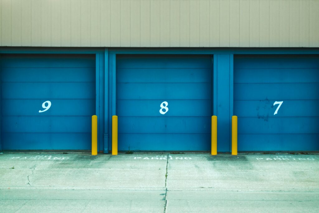 Three blue shutter doors numbered 9, 8, and 7 with yellow barriers in urban environment.
