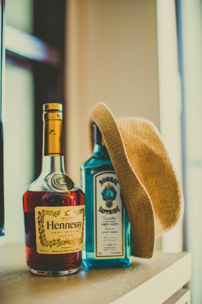 Stylish composition of Hennessy and Bombay Sapphire bottles with a straw hat.